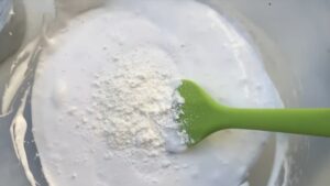 Baking Soda Sprinkled on Top of White Glue in A Bowl with A Green Spatula