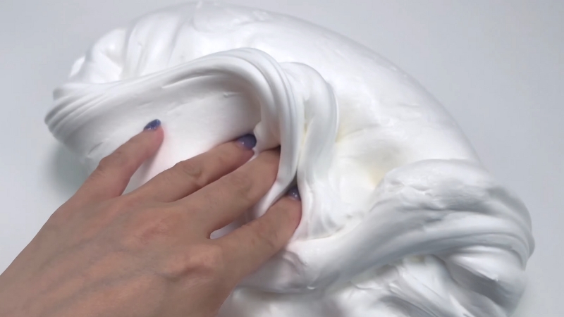 A Hand Pressing Into a Soft, Fluffy White Slime on A Smooth Surface